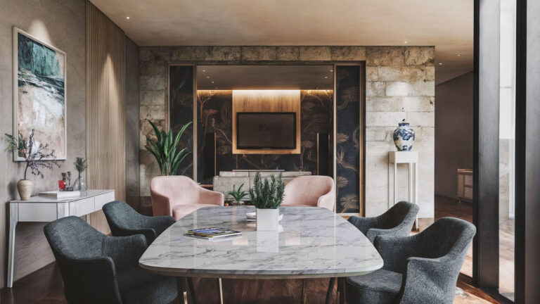 Image du salon après la rénovation par BYAA Inside à Bordeaux Pey-Berland. On y voit un lustre moderne, une table basse en marbre, des fauteuils en tissu et un mur en pierre naturelle.