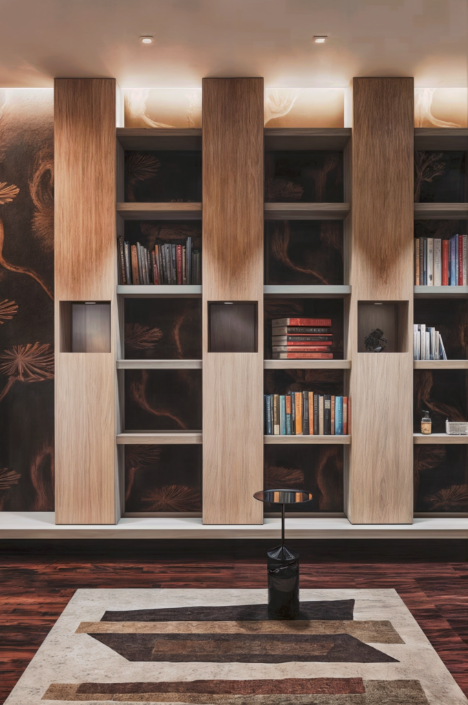 Image du salon avec bibliothèque après la rénovation par BYAA Inside à Bordeaux Pey-Berland. On y voit un mur avec du papier peint texturé, des étagères en bois intégrées, un canapé gris, un fauteuil noir et une table basse ronde.